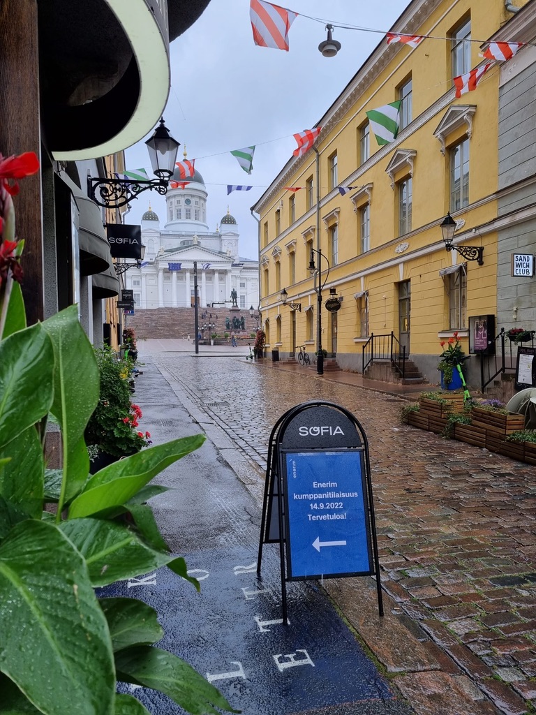 Kapealla, vanhalla, sateesta kostealla kadulla on kyltti, joka ohjaa Enerimin asiakastilaisuuteen, kadun päässä näkyy Helsingin Tuomiokirkko.