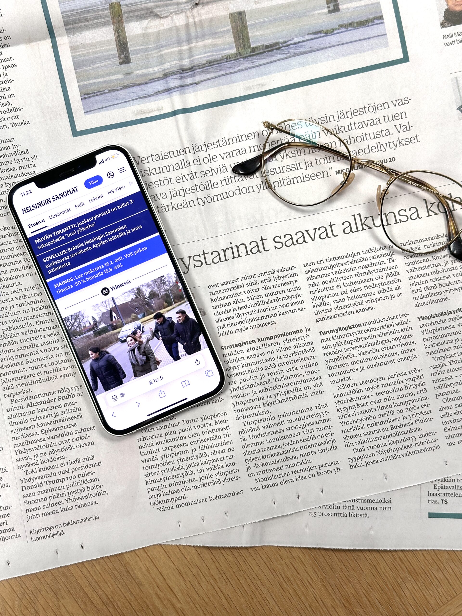 Sanomalehden sivun päällä on kännykkä ja silmälasit
